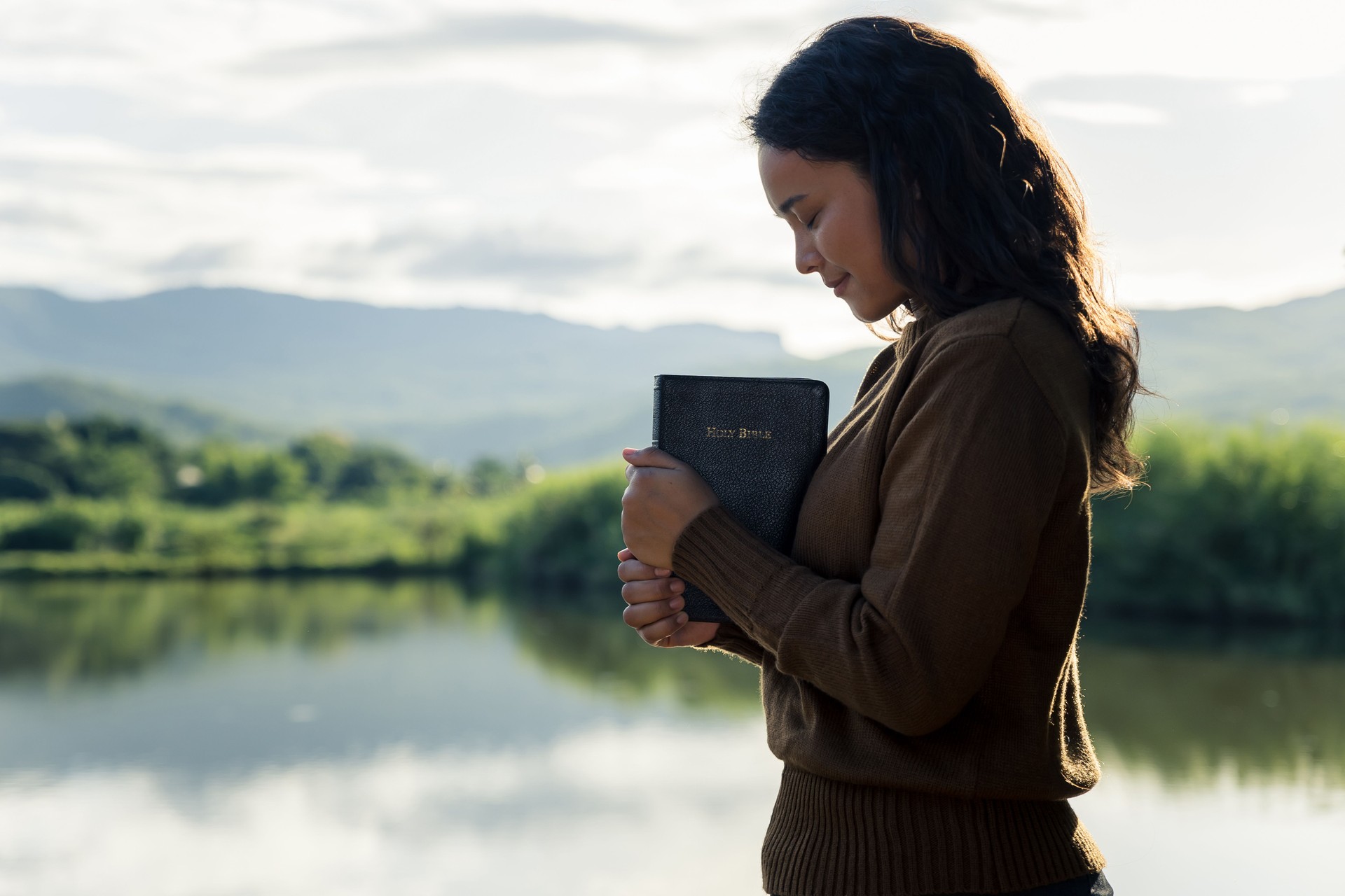 Young woman praying to god with the bible.